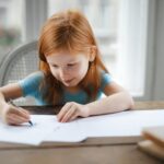A little girl is writing on paper at the table.